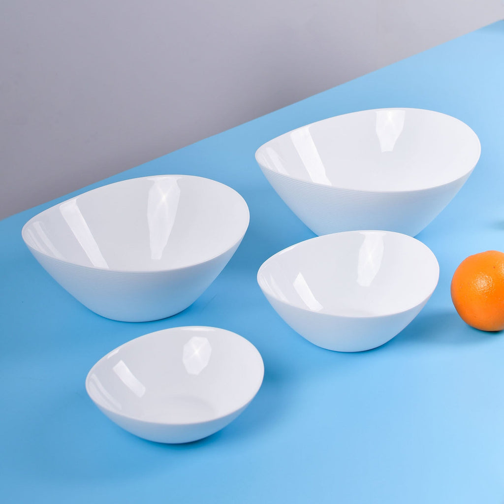 Four white opal glass bowls in different sizes arranged on a blue surface against a light gray background, with a small orange fruit near the right edge.