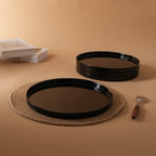 Four round black opal glass dinner plates, one in the front and the other three stacked in the back, displayed on a warm beige background.