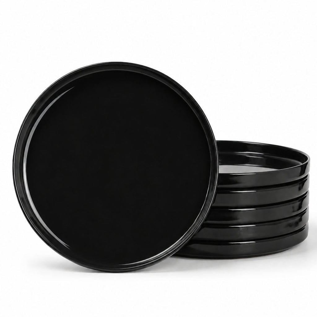 A set of glossy black round opal glass dinner plates, with one standing upright in front of a stack of five on a clean white background.
