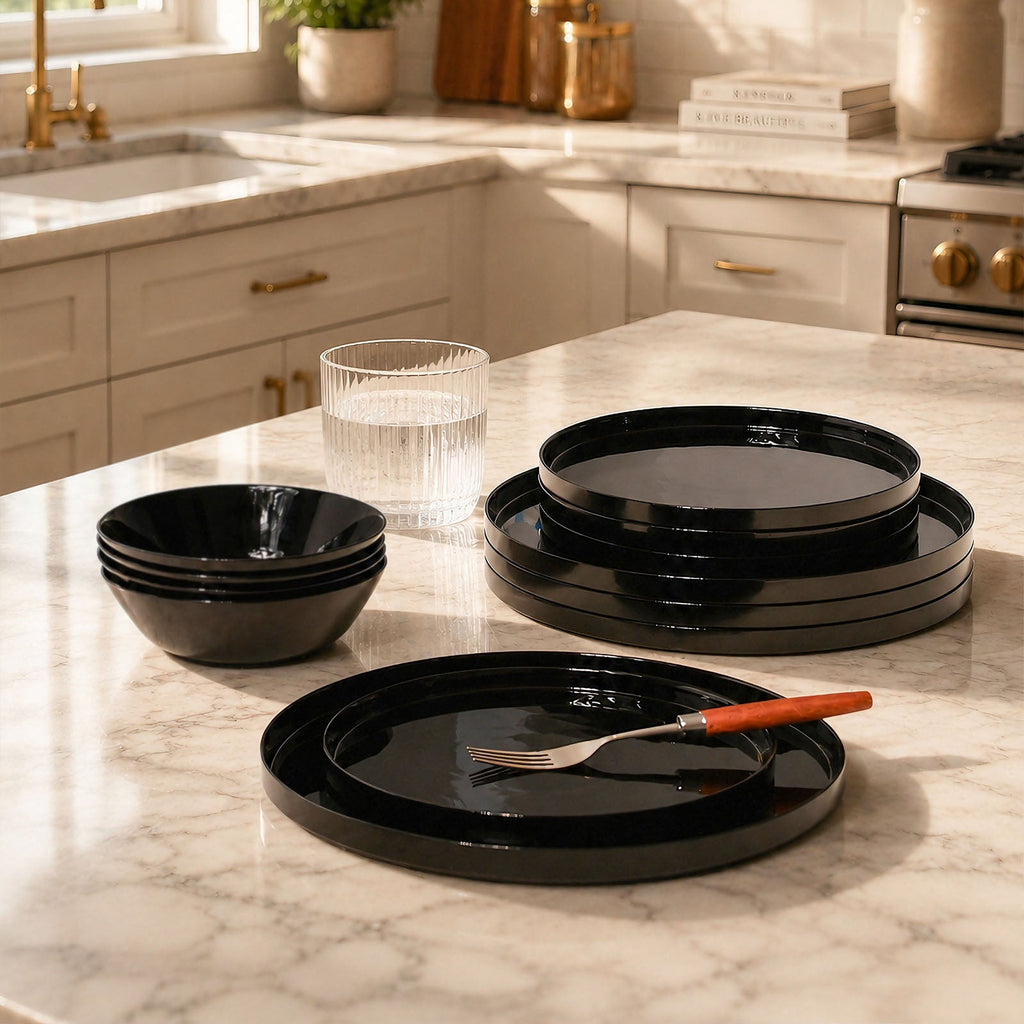 Black opal glass dinnerware set including plates and bowls arranged on a marble kitchen countertop, with a glass and a utensil in a real kitchen setting.